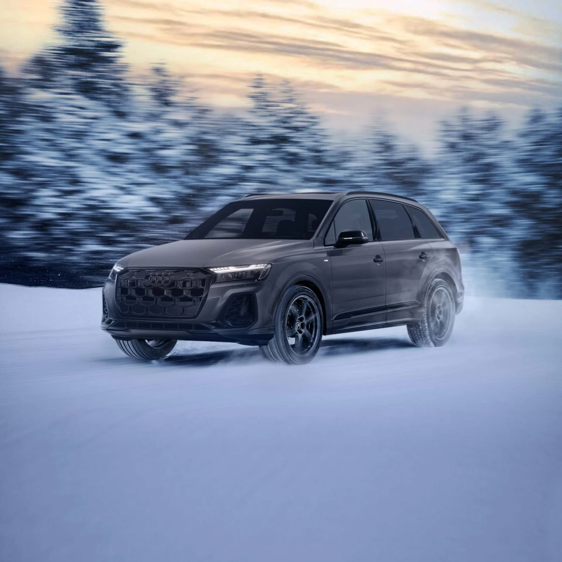 Audi Q7 gris foncé en mouvement sur route enneigée, forêt floue en arrière-plan