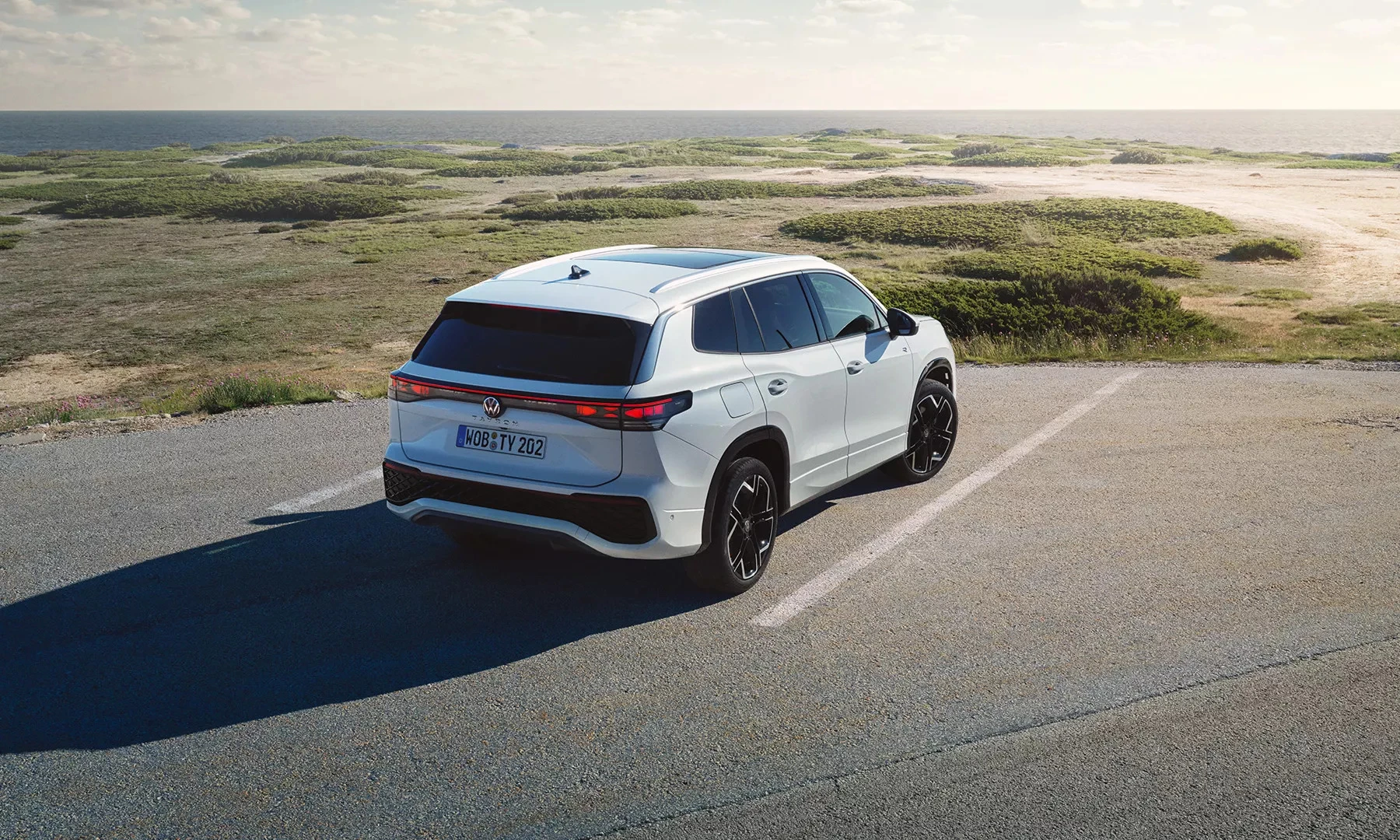 Volkswagen Tayron blanc stationné près de la mer, vu de trois-quarts arrière sur une route côtière