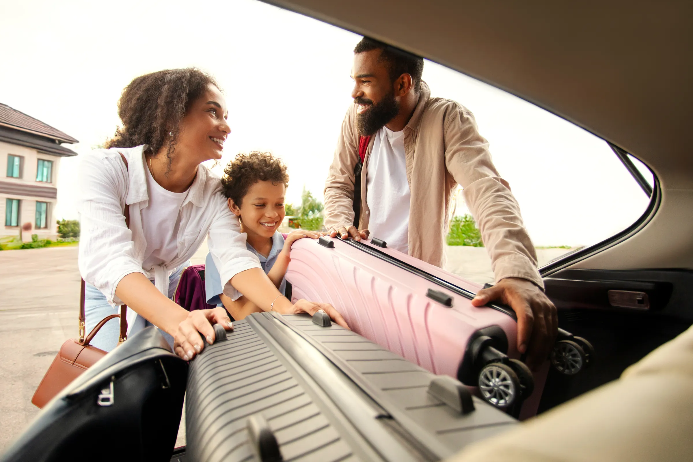 Parents et enfant rangeant une valise dans le coffre d’une voiture familiale