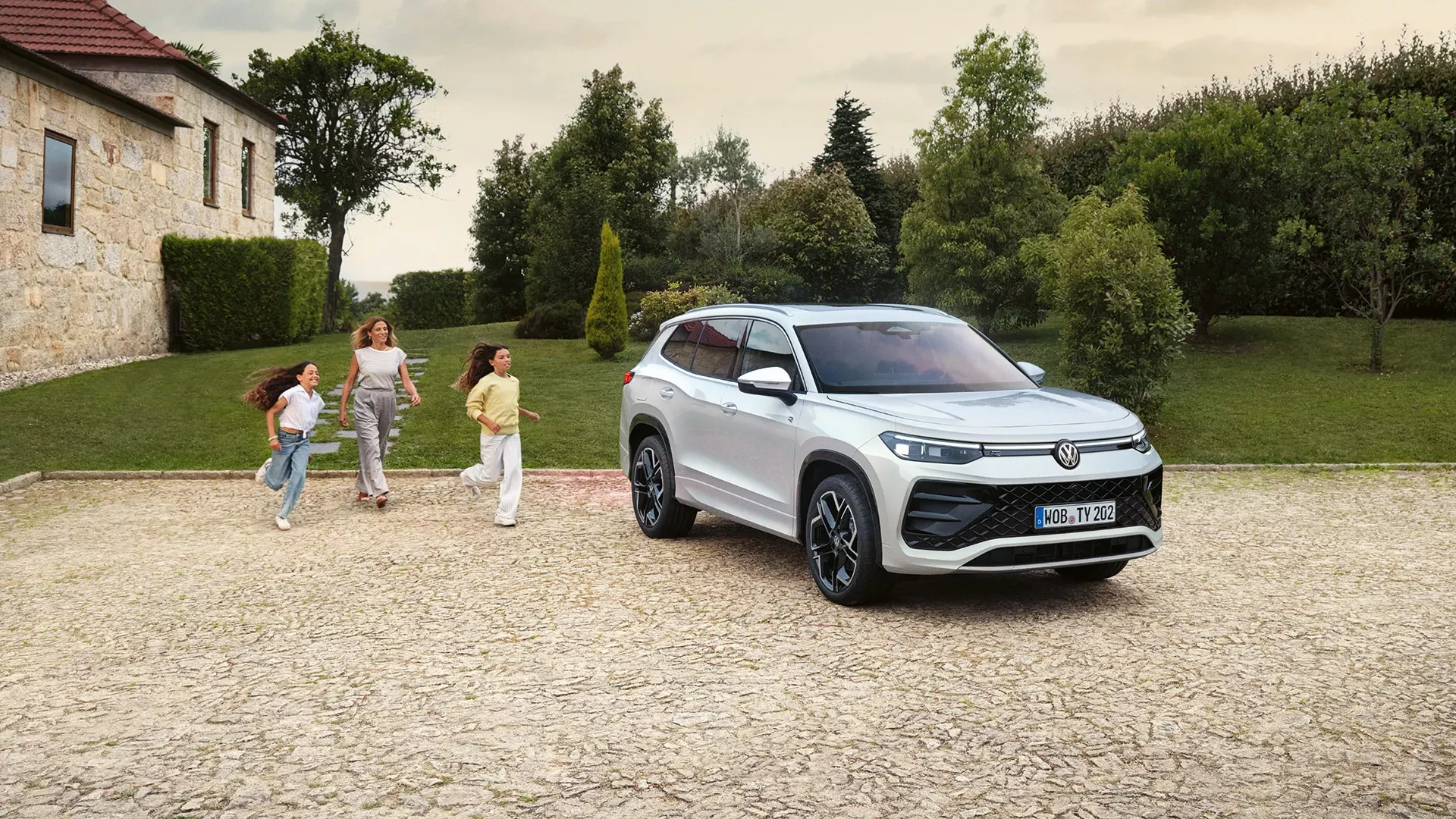 Famille qui court vers Volkswagen Tayron, grand SUV 7 places avec coffre généreux